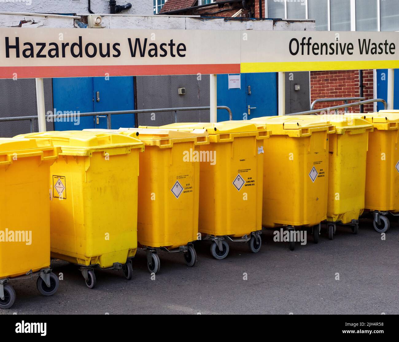 Gelbe Recycling-Behälter vor dem Teddington Memorial Hospital, SW London, Großbritannien; mit Anzeichen für gefährliche und anstößige Abfälle Stockfoto