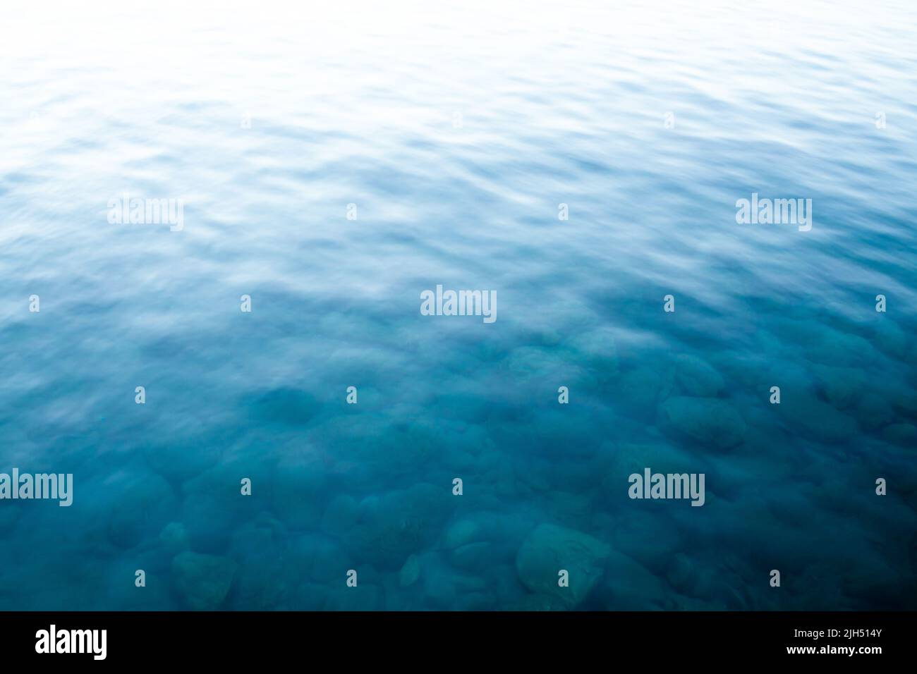 Blaue Wasseroberfläche. Türkisfarbene Meereswellen. Transparentes Meerwasser mit Felsen am Boden. Unschärfe-Bild für den Hintergrund. Wellenstruktur. Verschwommenes Bild Stockfoto