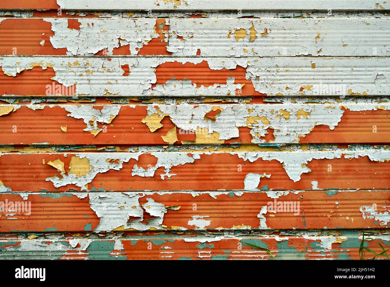 Schichten von Creme-, Orange- und Grünfarbe lösen sich von einer Metalloberfläche Stockfoto