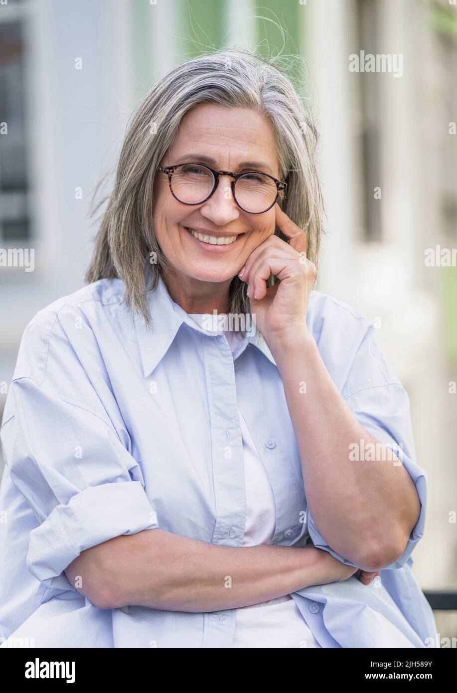 Porträt von schönen reifen grauen Haaren Frau trägt Brille im Freien stehend genießen Freizeit Urlaub rund um die Welt im Ruhestand reisen. Reife Frau mit perfekter Haut trägt blaues Hemd. Stockfoto