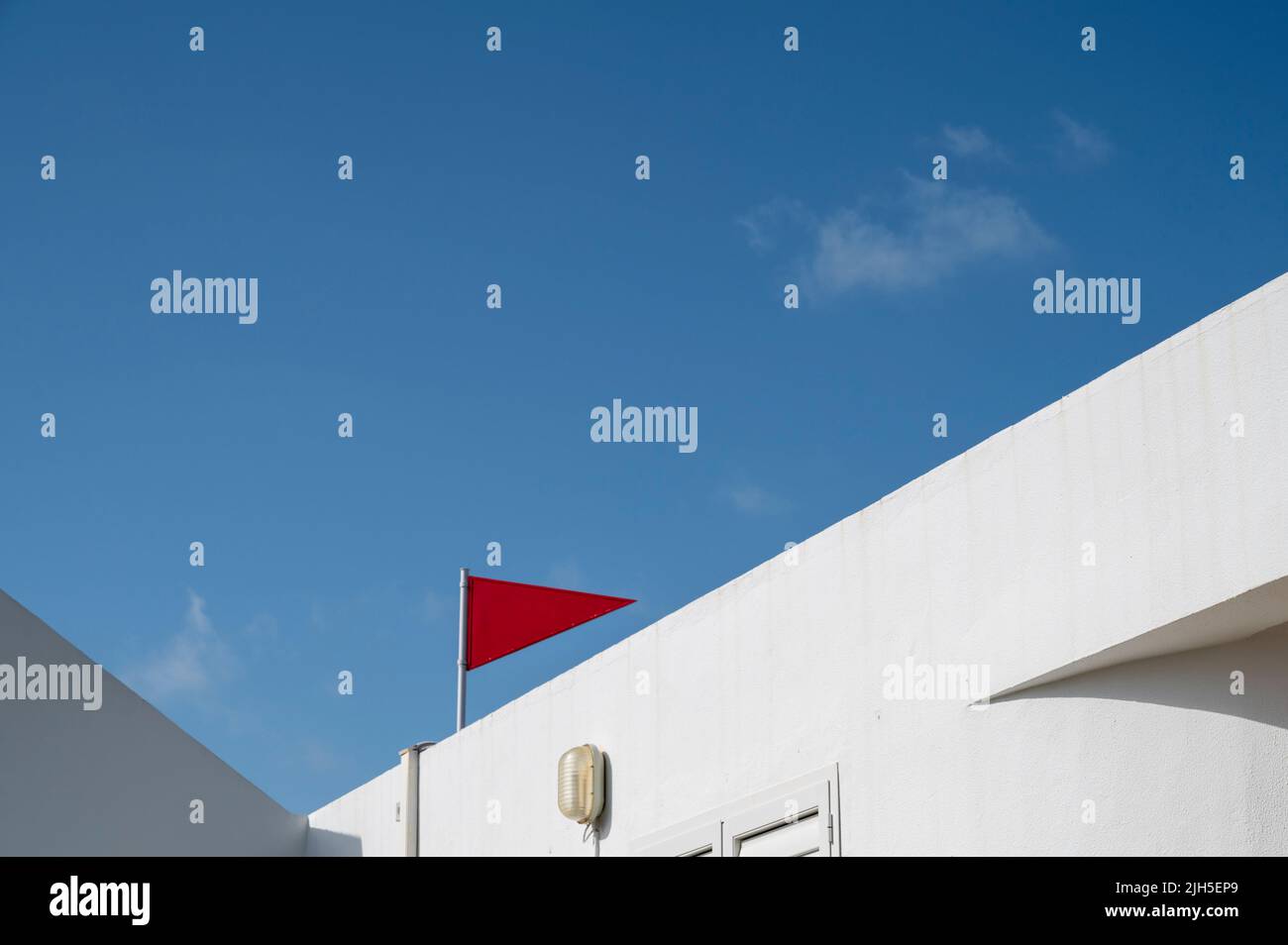 Eine rote Flagge auf einem Gebäude in Spanien vor einem blauen Himmel in einem farbenfrohen Bild der städtischen Architektur Stockfoto