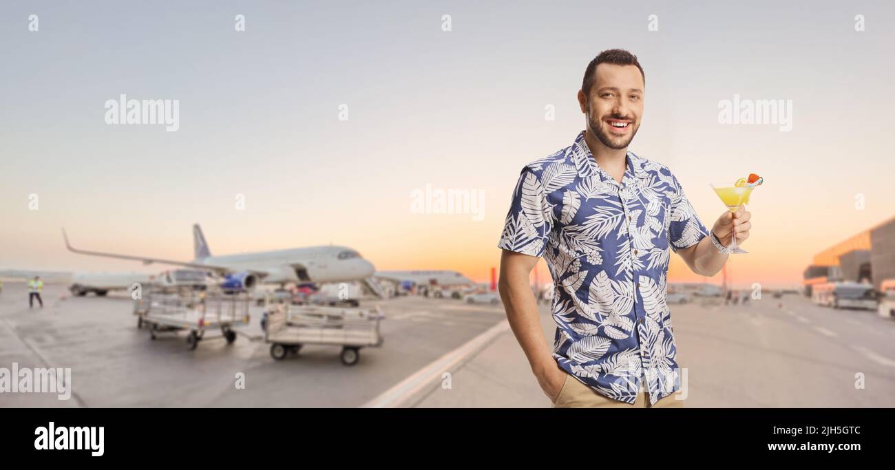 Mann mit einem Cocktail, der mit Flugzeugen auf einem Flughafenvorfeld posiert Stockfoto