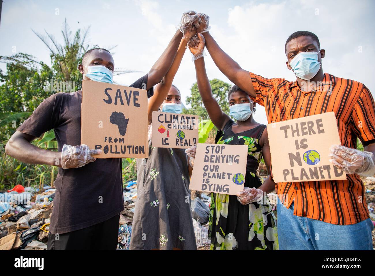 Vier junge Erwachsene protestieren mit Zeichen gegen die Verschmutzung vor einer illegalen offenen Deponie in Afrika Stockfoto