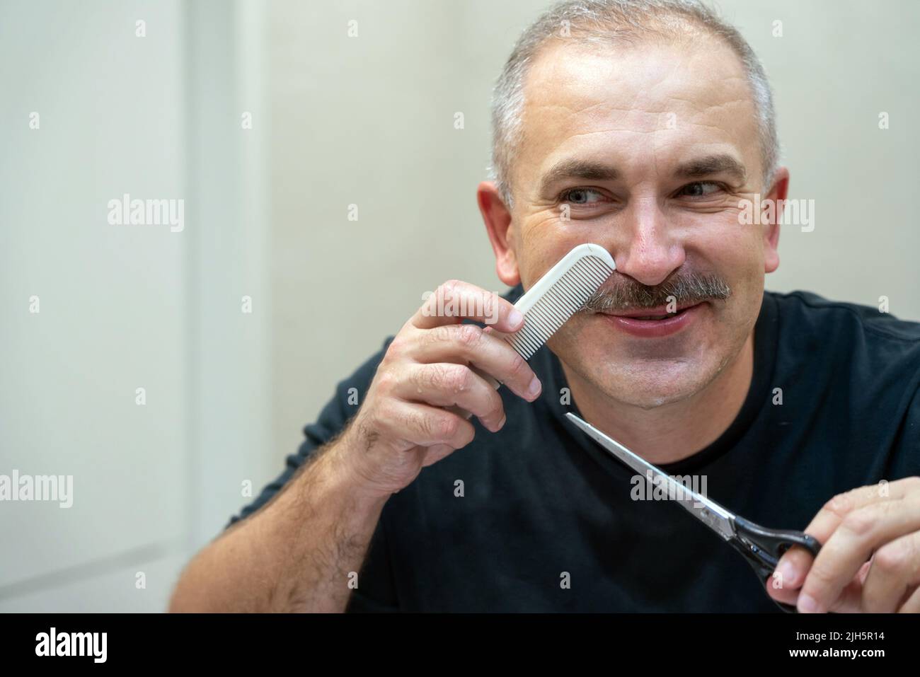 Gutaussehender Mann mittleren Alters, der mit einer Schere seinen Schnurrbart Schnitt Stockfoto