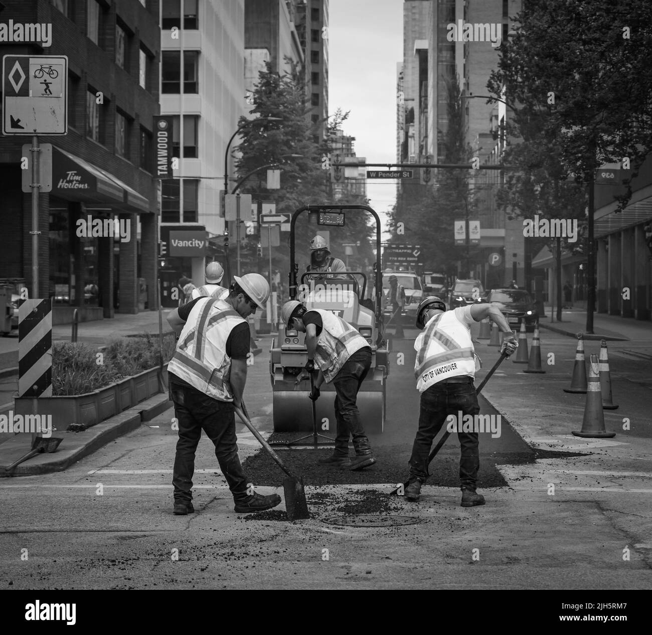 Ein Team von Arbeitern legte den heißen Asphalt auf eine Straße. Straßenbauarbeiter mit Schaufeln in Schutzuniformen. Straßenbauarbeiten in einer Stadt-Juli 1 Stockfoto