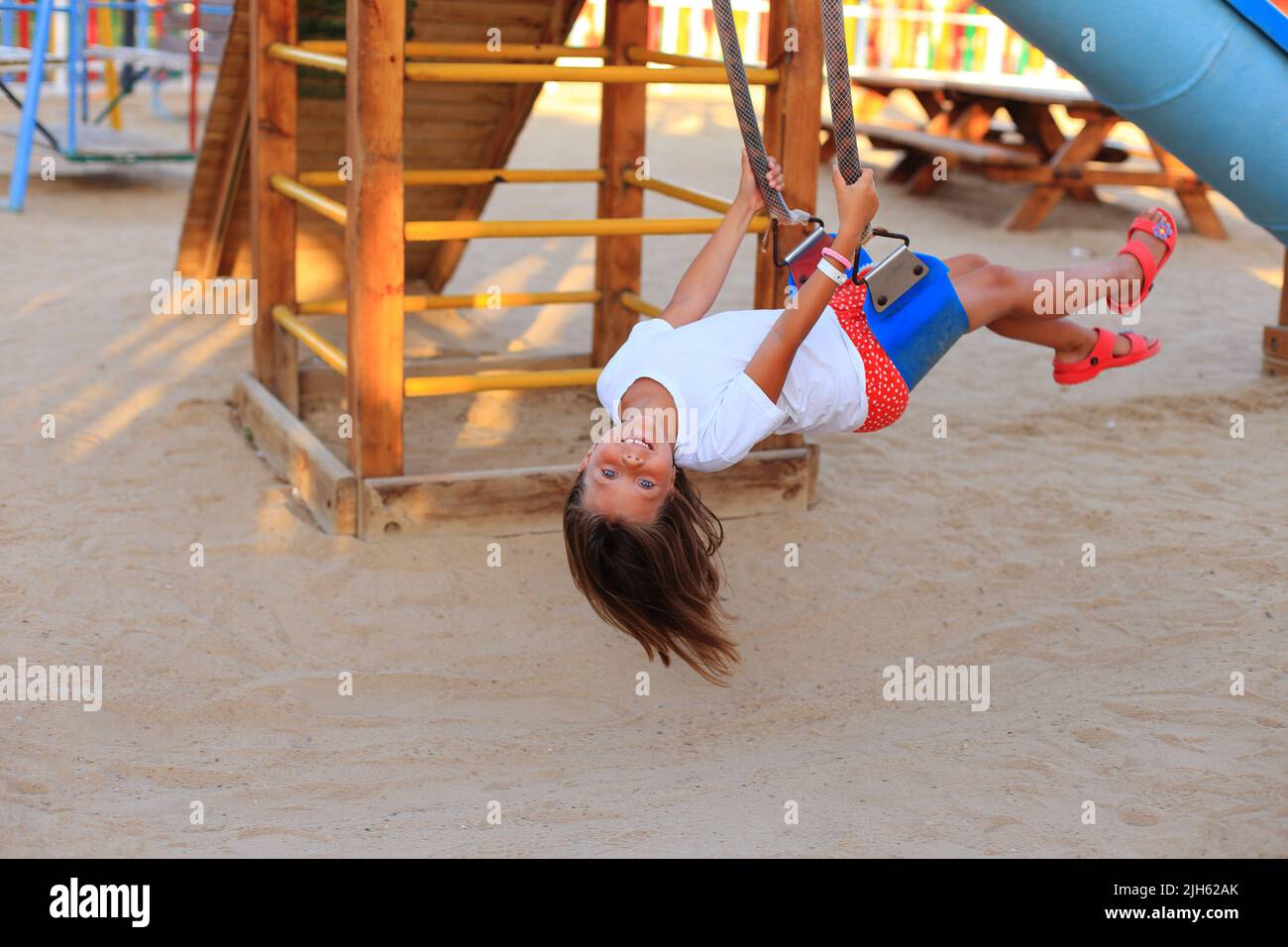 Das Mädchen reitet auf einer Schaukel auf dem Spielplatz. Karussells für Kinder im Freien Stockfoto