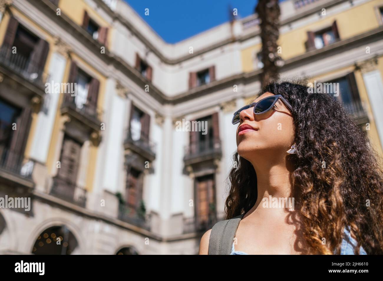 Junge, dunkelhaarige Frau mit Sonnenbrille schaut weg. Sie hat einen verschwommenen Hintergrund von alten Gebäuden. Stockfoto