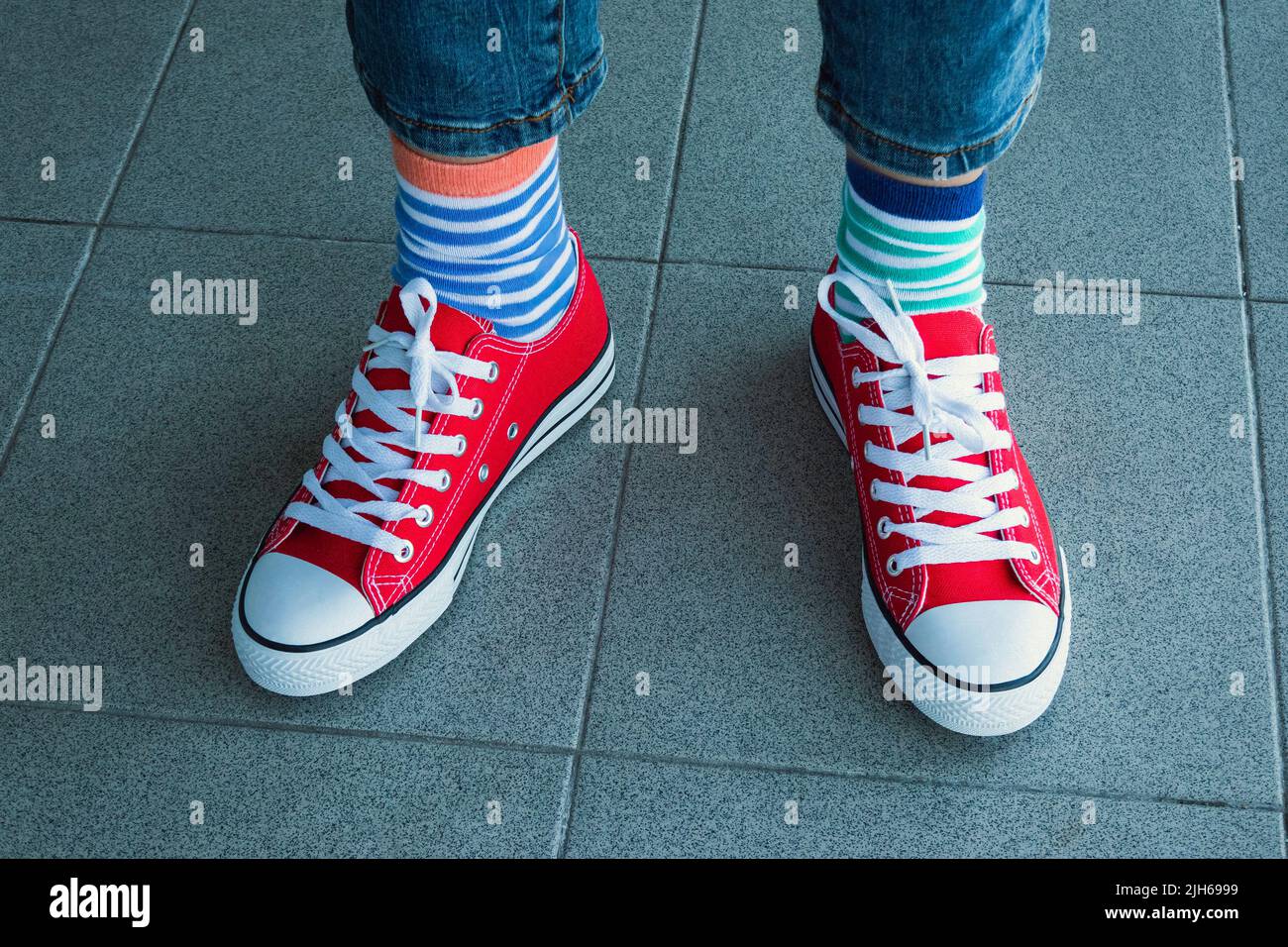 Kind trägt verschiedene Socken. Kinderbeine in unpassenden Socken auf grauem Hintergrund. Tag der ungeraden Socken, Woche der Anti-Mobbing-Bekämpfung. Down-Syndrom-Bewusstsein Stockfoto