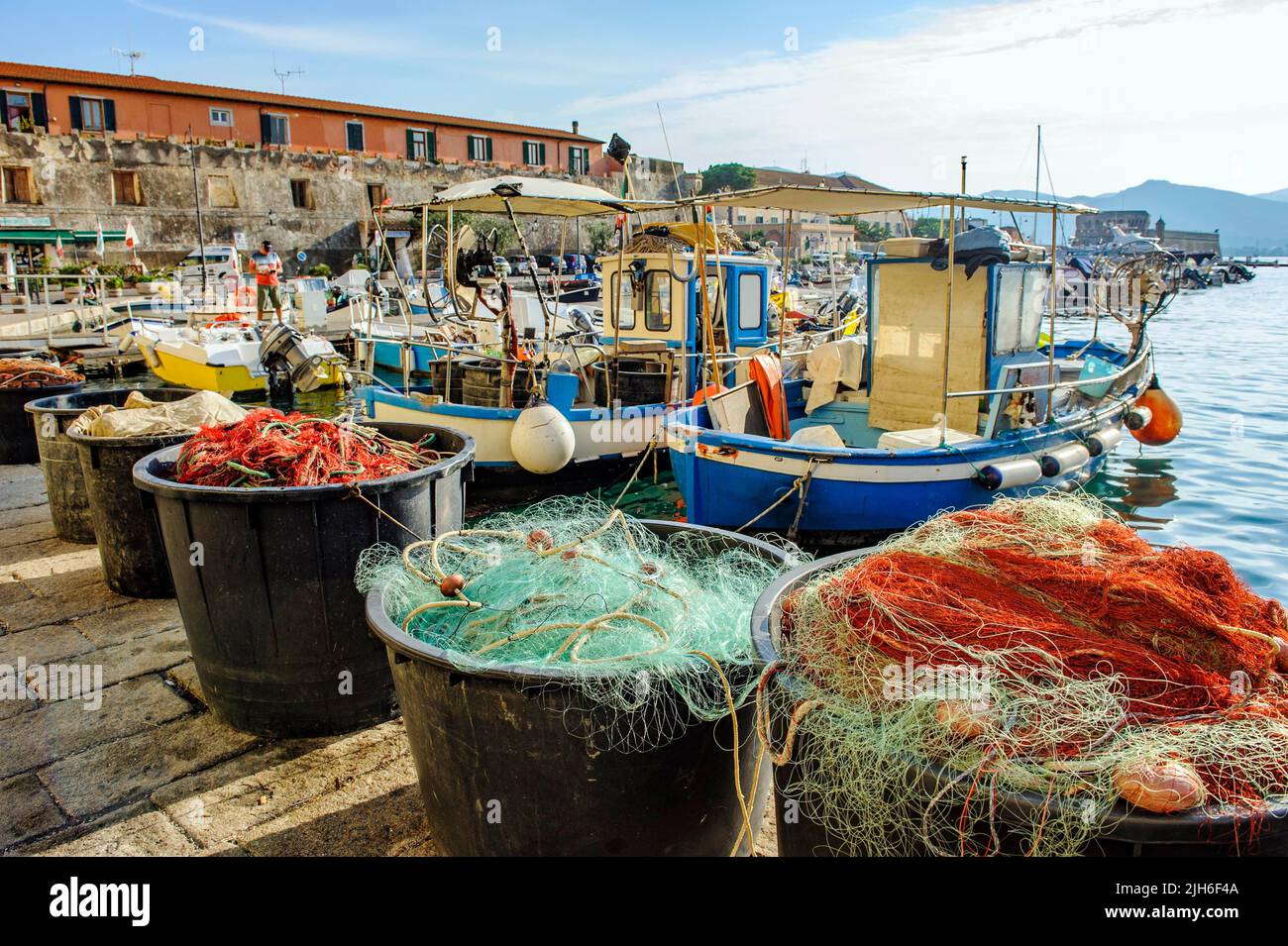 Becken mit roten und grünen Fischernetzen, dahinter kleine Fischerboote, die am Kai des alten Hafens von Portoferraio, Portoferraio, Elba festgemacht sind Stockfoto