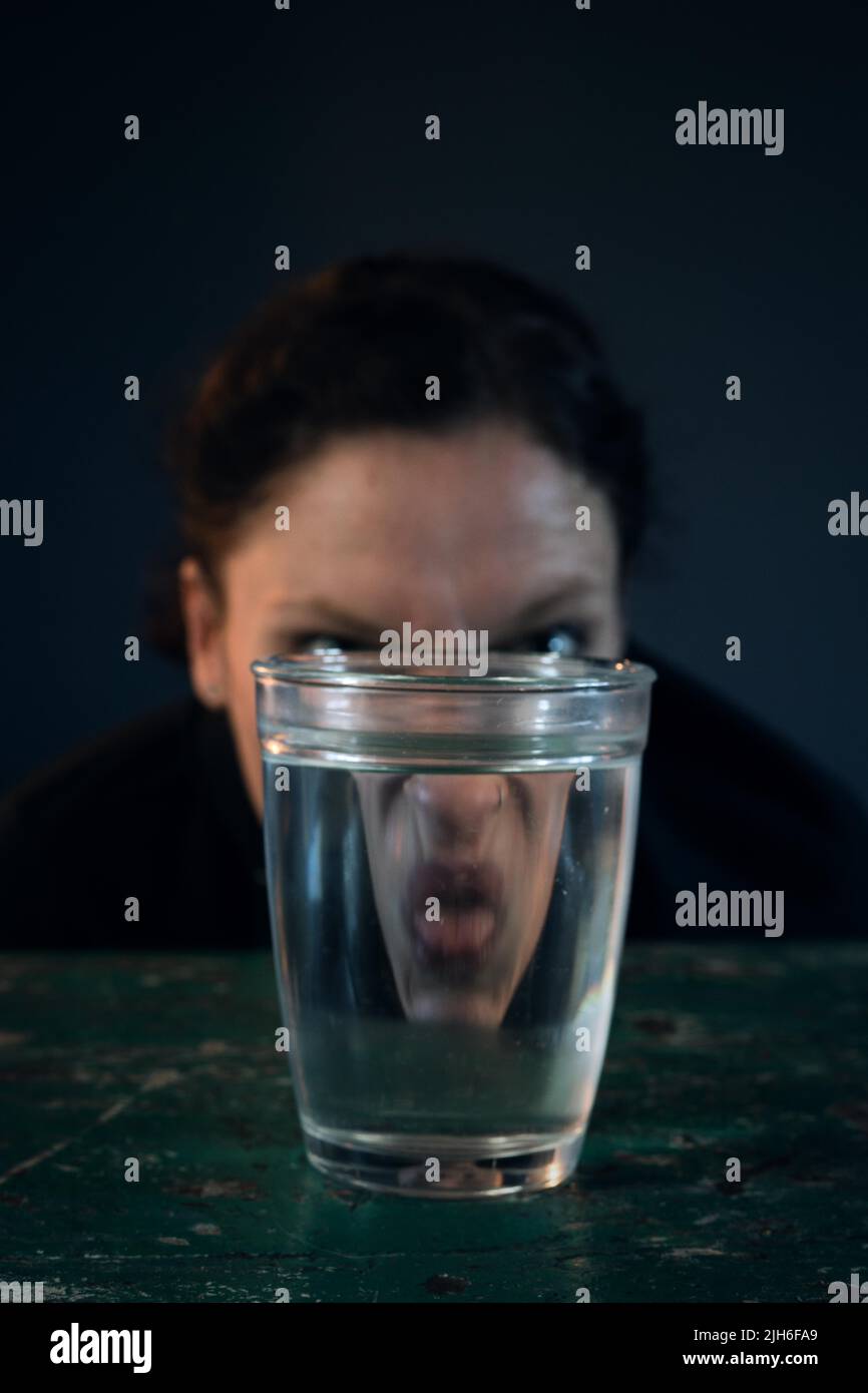Das zornige Gesicht einer Frau spiegelte sich in einem Glas Wasser wider Stockfoto