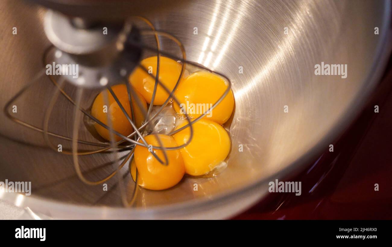 Rohe Eier in einer Metallschüssel mit stehendem Mixer. Eigelb mit Zucker in der Küchenarmatur zubereiten Stockfoto