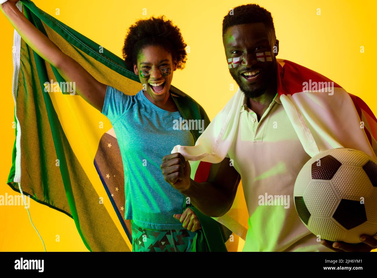 Bild eines afroamerikanischen Fußballfans-Paares mit Flaggen brasiliens und englands in gelbem Blitz Stockfoto