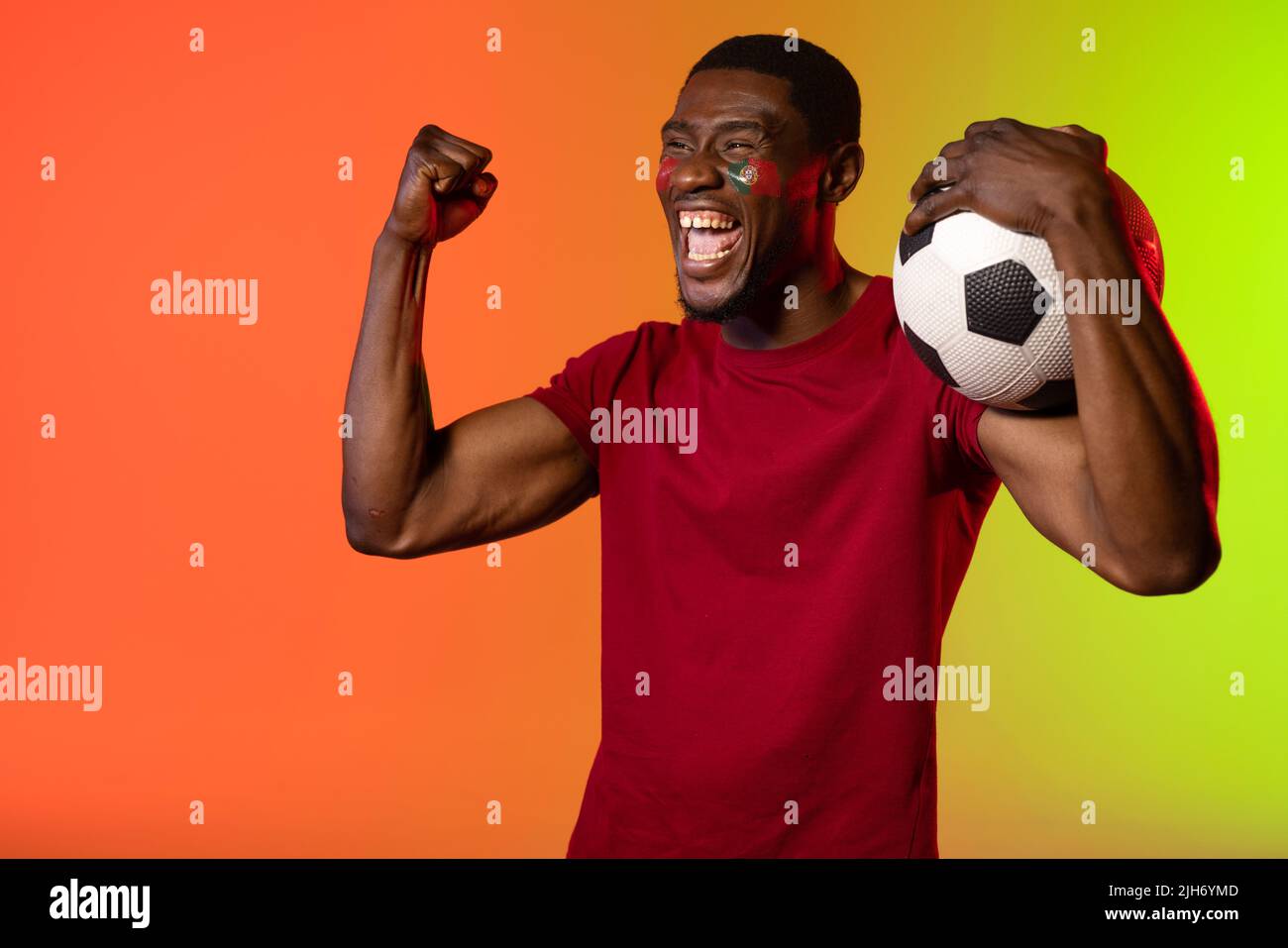 Fröhlicher afroamerikanischer Fußballfan mit Flagge portugals auf den Wangen über orangefarbenem Licht Stockfoto