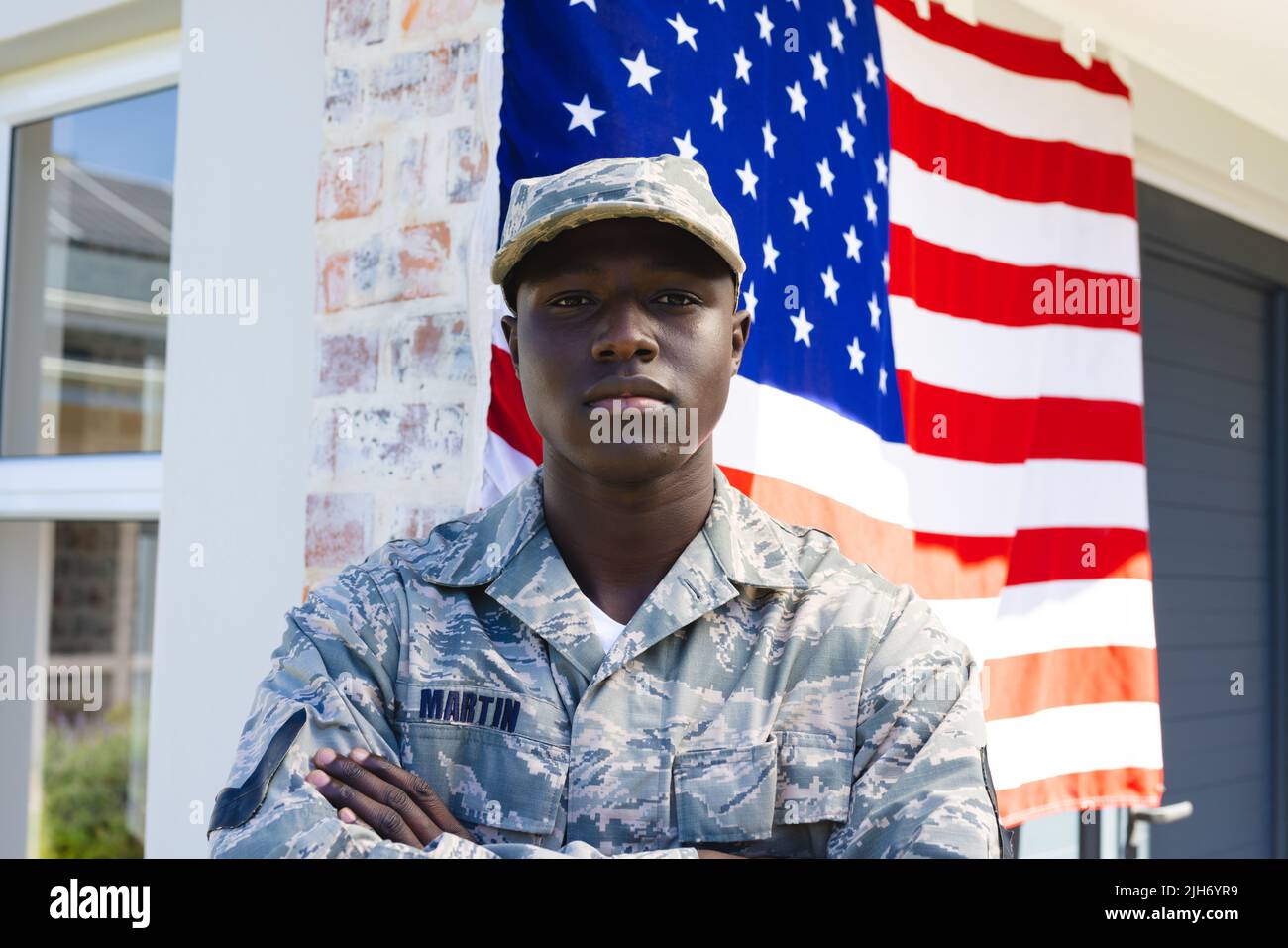 afroamerikanischer Soldat der mittleren Erwachsenen-Armee in Tarnkleidung mit Waffen, die gegen die Flagge gekreuzt sind Stockfoto