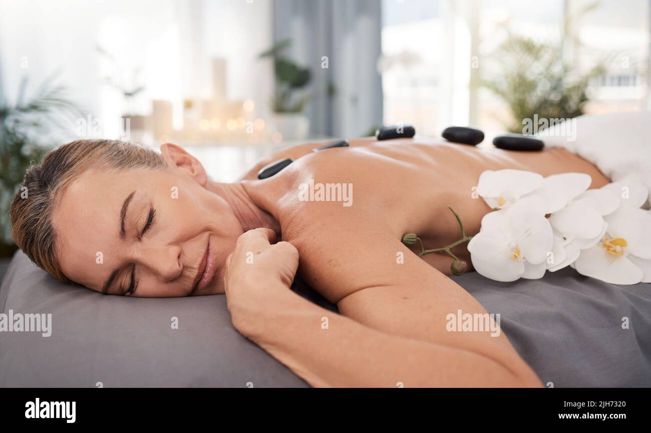 Heiße Steine beruhigen die Psyche und absorbieren Giftstoffe. Aufnahme einer reifen Frau, die eine entspannende Hot Stone Massage in einem Spa genießt. Stockfoto