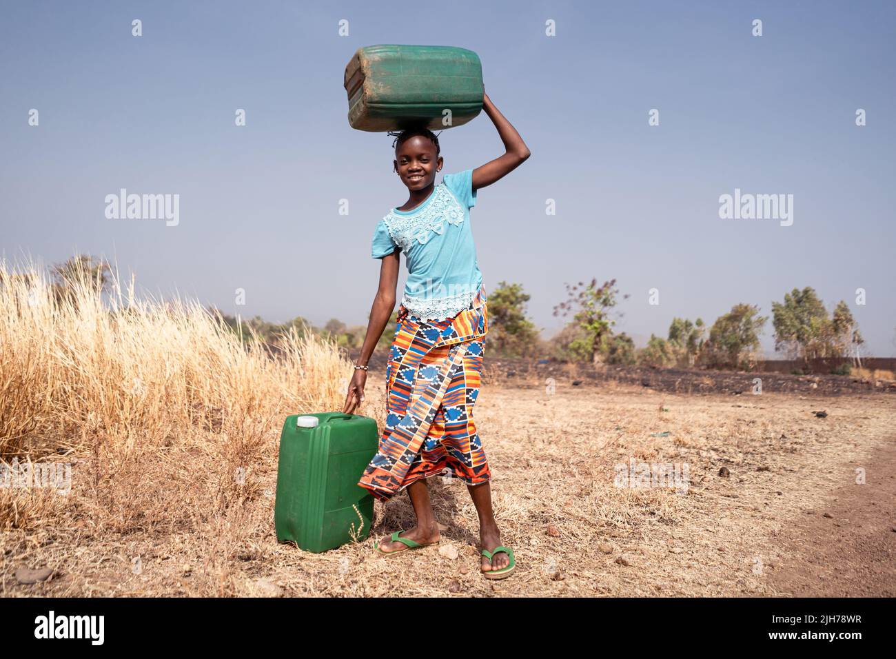 Niedliches kleines westafrikanisches Mädchen mit Wasserbehältern; Symbol für das Fehlen von Wasserinfrastruktur in vielen armen afrikanischen Dörfern Stockfoto