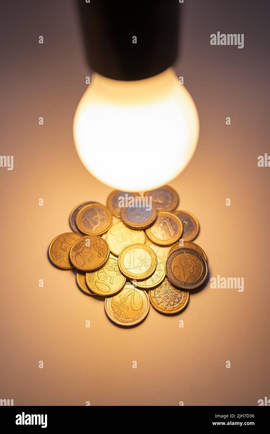 Glühbirne beleuchtet leuchtende Münzen für die hohen Kosten für Strom und Inflation. Stockfoto