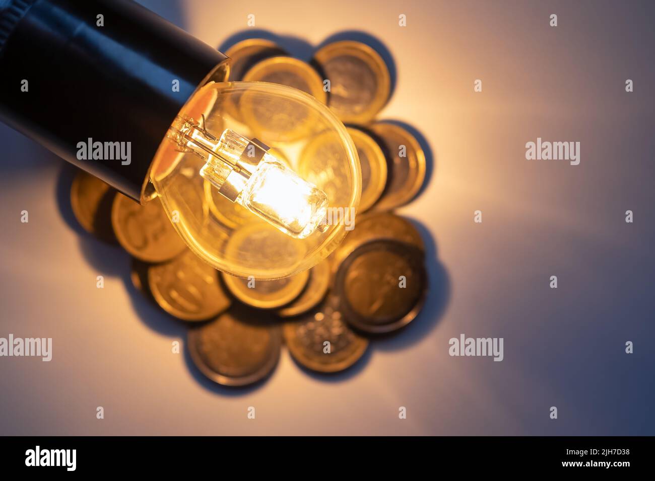Verbrauchsarme ökologische Glühbirne auf Münzen, die die hohen Stromkosten darstellen. Stockfoto