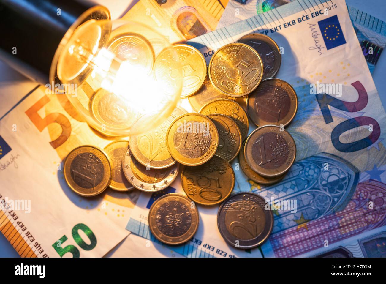 Glühbirne, die auf Münzen und Geldscheinen leuchtet, was die hohen Kosten für Strom darstellt. Stockfoto