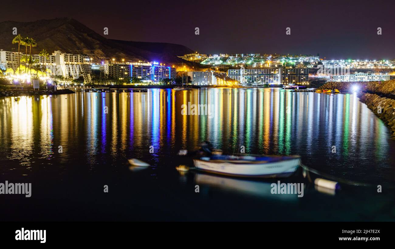 Nachtfoto der Küste von Gran Canaria mit nachts beleuchteten Gebäuden und Hotels und Reflexionen der Lichter im Meerwasser. Stockfoto