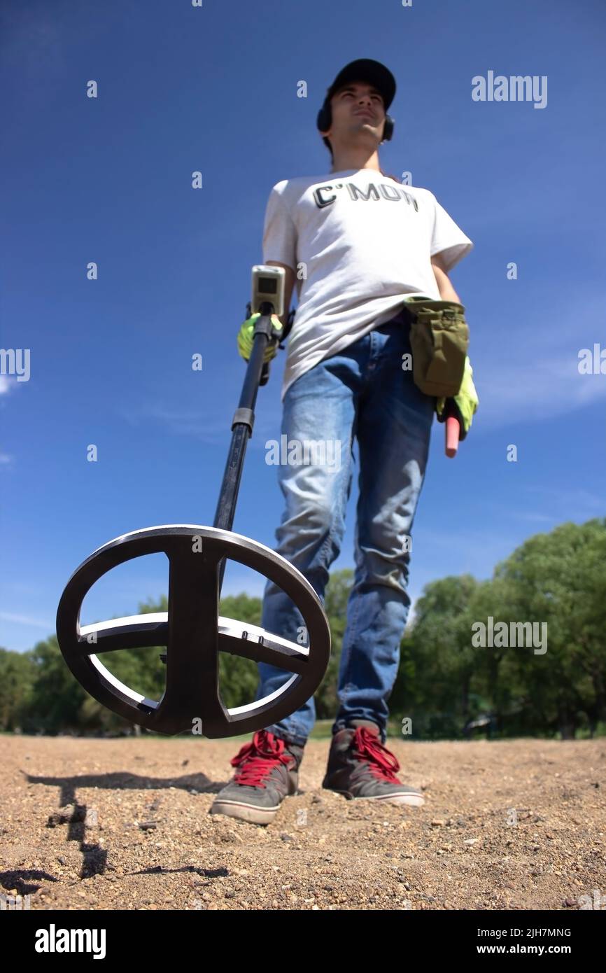 Ein Typ mit kabellosen Kopfhörern hält einen drahtlosen Metalldetektor in der Hand am Strand Stockfoto