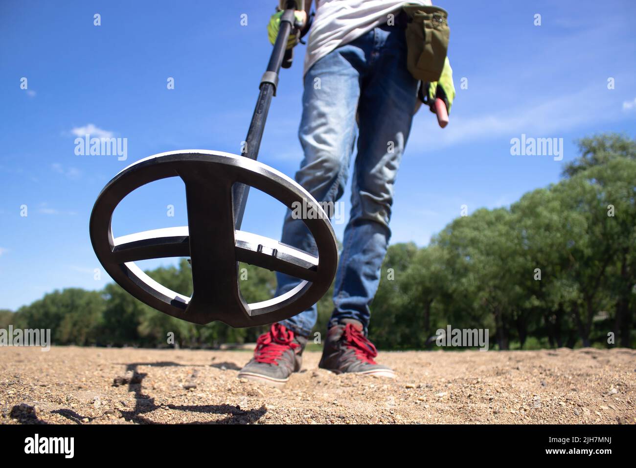 Ein Typ mit kabellosen Kopfhörern hält einen drahtlosen Metalldetektor in der Hand am Strand Stockfoto