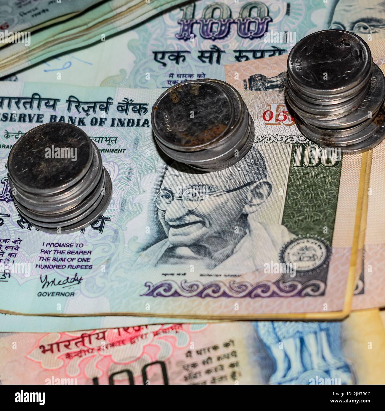 Seltene alte indische Bankrupien-Münzen fallen auf Geldscheine, fallen nach unten indische Rupien-Münzen auf hundert Rupien-Banknoten, indische Währungsmünzen fallen Stockfoto