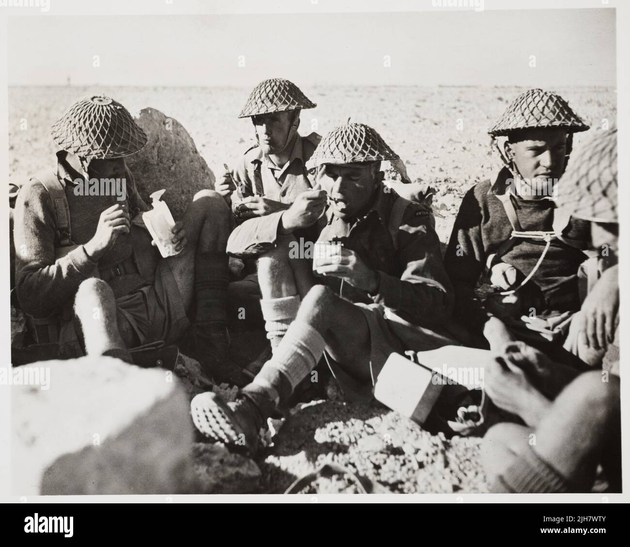 Ein Vintage-Foto aus der Zeit um 1942, das den Vizegoutenant Charles Hazlitt Upham und Soldaten der neuseeländischen Division in der westlichen Wüste zeigt, die Feldrationen essen. Im Zentrum steht der Vizeleutnant Charles Hazlitt Upham, der für seine Kämpfe auf Kreta und in El Alamein Nordafrika während des Zweiten Weltkriegs mit dem V.C. und der Bar ausgezeichnet wurde. Er war einer von nur drei Personen, die zweimal das Victoria-Kreuz erhielten Stockfoto