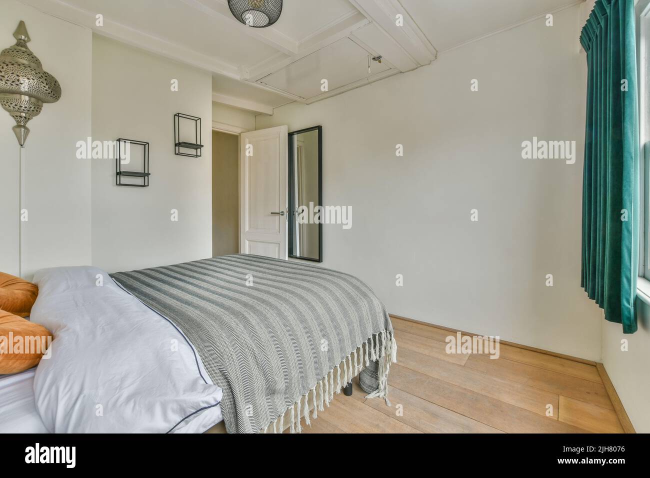 Komfortables Bett und Lampe in einem kleinen, schmalen, minimalistischen Schlafzimmer mit weißen Wänden und Fenster in einem modernen Apartment untergebracht Stockfoto