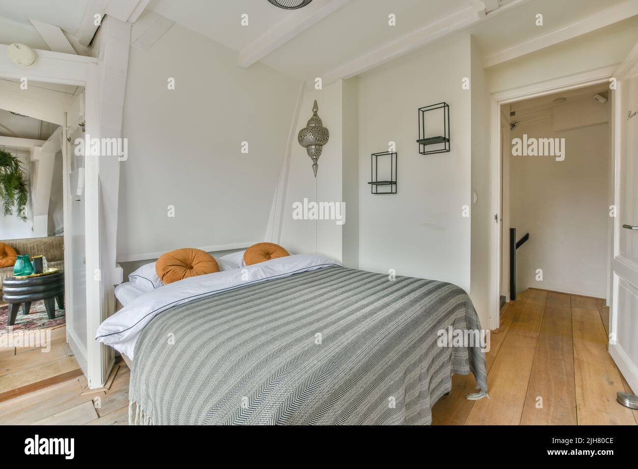 Komfortables Bett und Lampe in einem kleinen, schmalen, minimalistischen Schlafzimmer mit weißen Wänden und Fenster in einem modernen Apartment untergebracht Stockfoto
