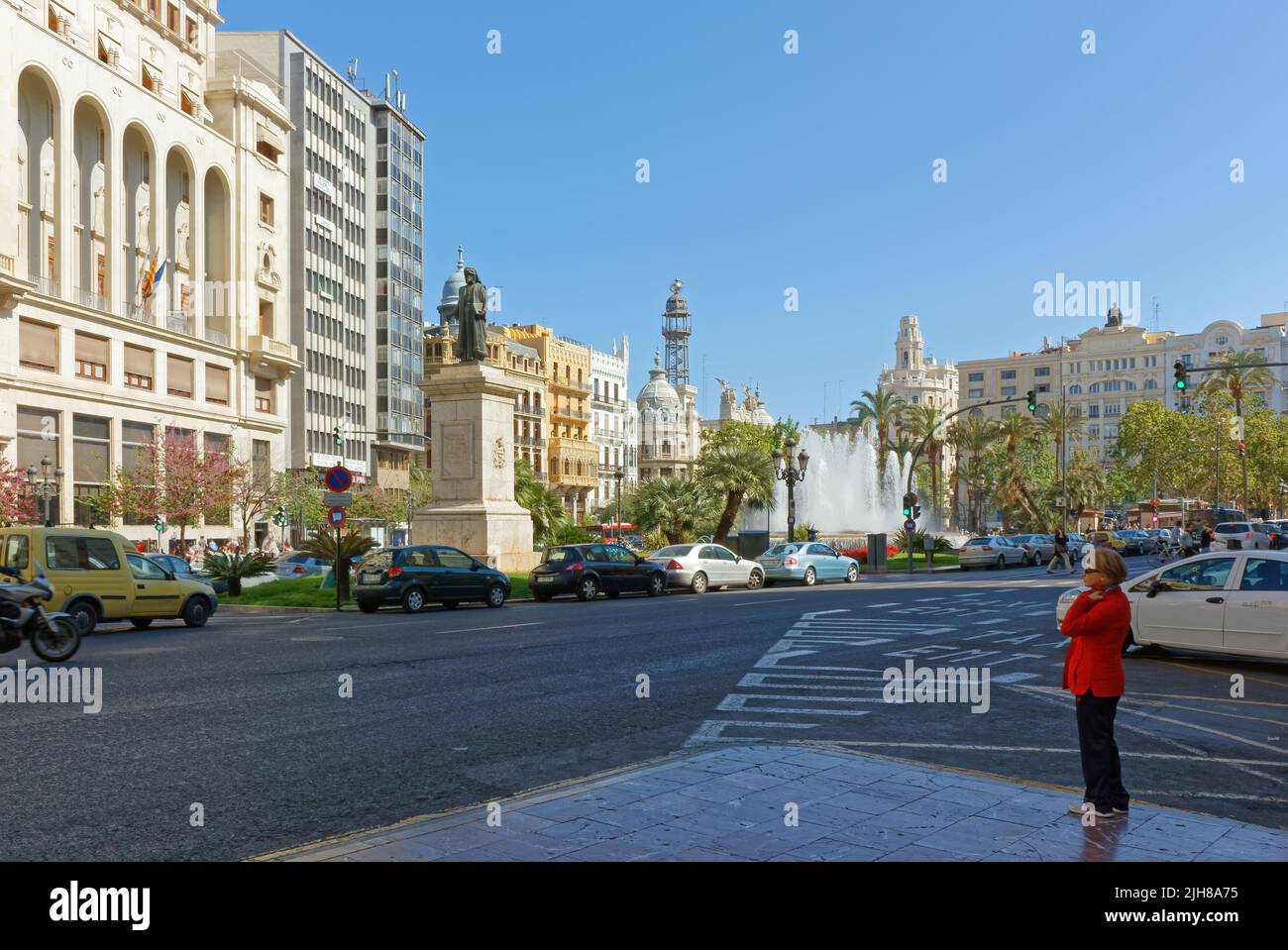 VALENCIA, Spanien - 23. April 2014: Eine blonde Frau mit rotem Mantel steht auf dem Bürgersteig in der Nähe der Plaza de l'Ajuntamiento im Stadtzentrum Stockfoto