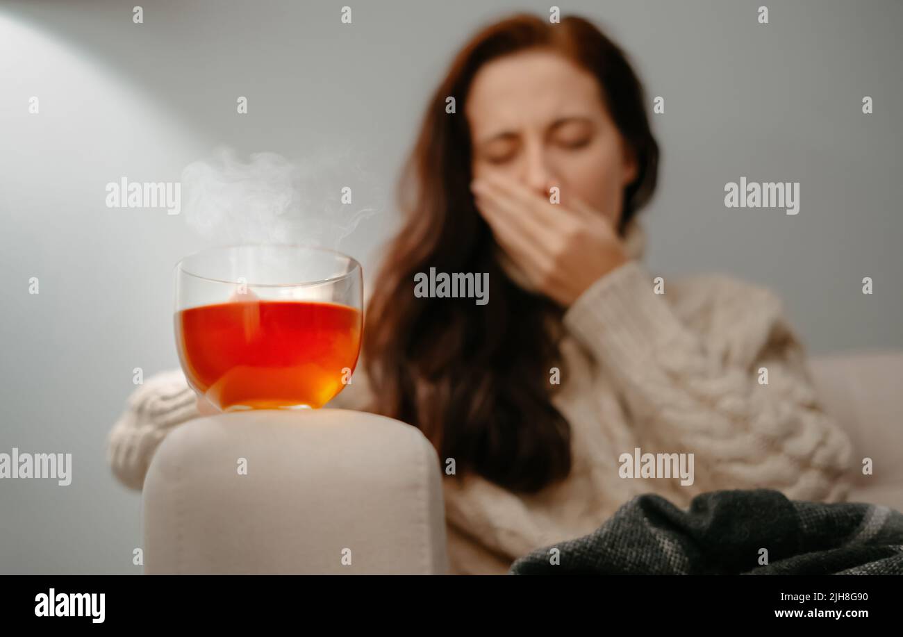Frau hustet in der Hand mit Halsschmerzen und hält heißen medizinischen Tee. Stockfoto