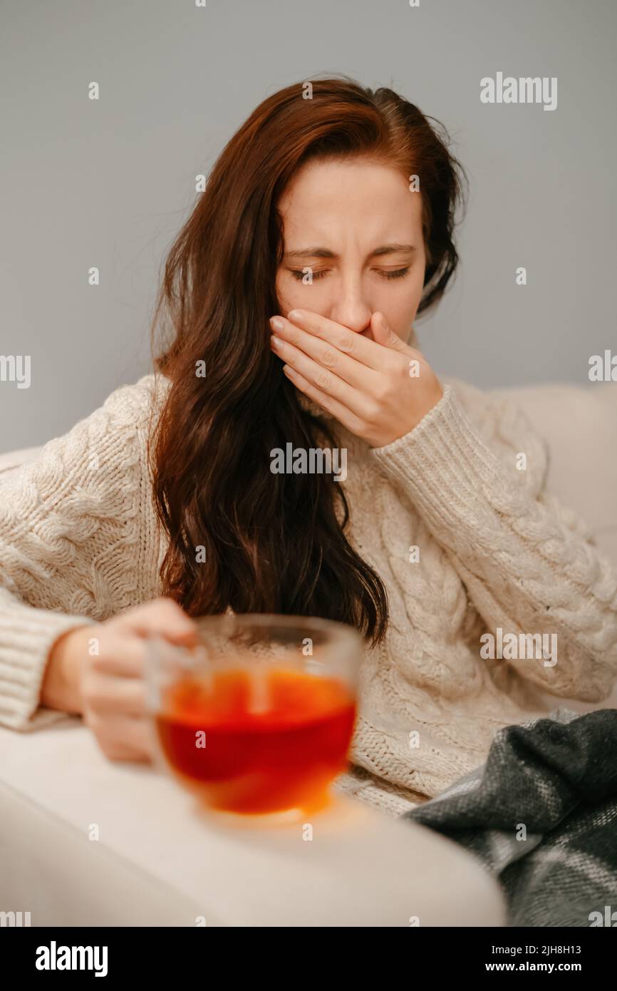 Eine Frau hustet von einem Halsschmerzen, der ihr Gesicht mit der Hand bedeckt. Stockfoto