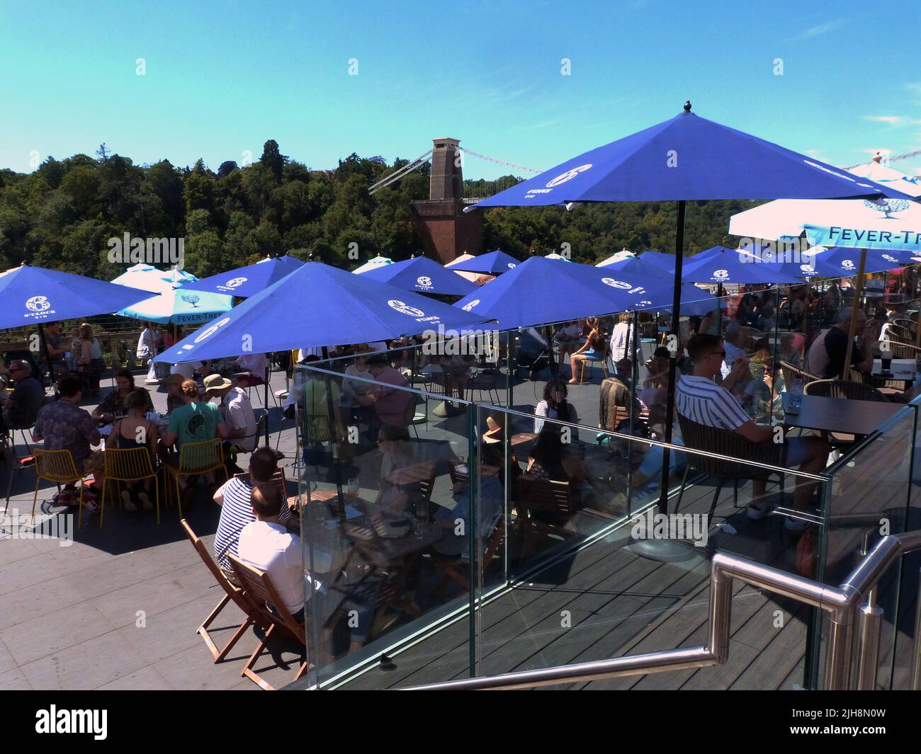 Die berühmte Clifton Suspension Bridge an einem sonnigen Sonntagnachmittag. Das ursprünglich von Isambard Kingdom Brunel entworfene und 1835 eröffnete Hotel erstreckt sich über die Avon-Schlucht über dem Fluss Avon in Clifton, Bristol. Es ist die bekannteste Struktur von Bristol und ist 365 Tage im Jahr geöffnet, mit einer Maut von £1,00, die mit einem Fahrzeug zu überqueren ist. Die Terrassenlage des Avon Gorge Hotels zieht einen konstanten Zustrom von Besuchern an, die den Blick auf dieses historische denkmalgeschützte Gebäude aus dem Jahr 1 genießen, während sie Erfrischungen unter schattigen Tischbrolles von diesem beliebten Aussichtspunkt genießen. Stockfoto