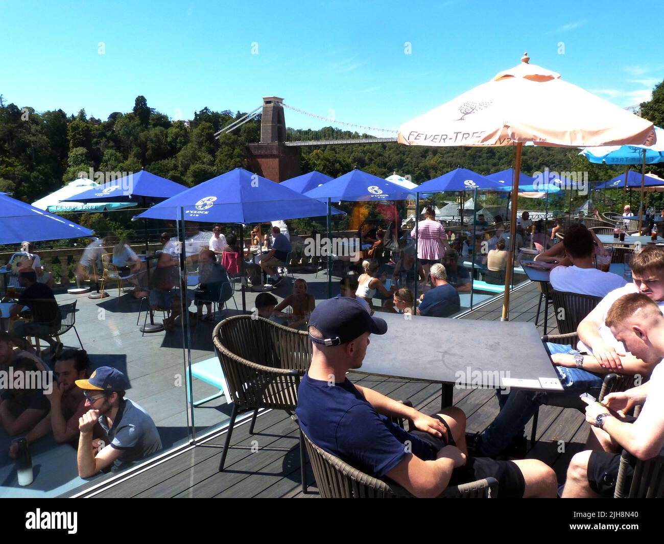 Die berühmte Clifton Suspension Bridge an einem sonnigen Sonntagnachmittag. Das ursprünglich von Isambard Kingdom Brunel entworfene und 1835 eröffnete Hotel erstreckt sich über die Avon-Schlucht über dem Fluss Avon in Clifton, Bristol. Es ist die bekannteste Struktur von Bristol und ist 365 Tage im Jahr geöffnet, mit einer Maut von £1,00, die mit einem Fahrzeug zu überqueren ist. Die Terrassenlage des Avon Gorge Hotels zieht einen konstanten Zustrom von Besuchern an, die den Blick auf dieses historische denkmalgeschützte Gebäude aus dem Jahr 1 genießen, während sie Erfrischungen unter schattigen Tischbrolles von diesem beliebten Aussichtspunkt genießen. Stockfoto