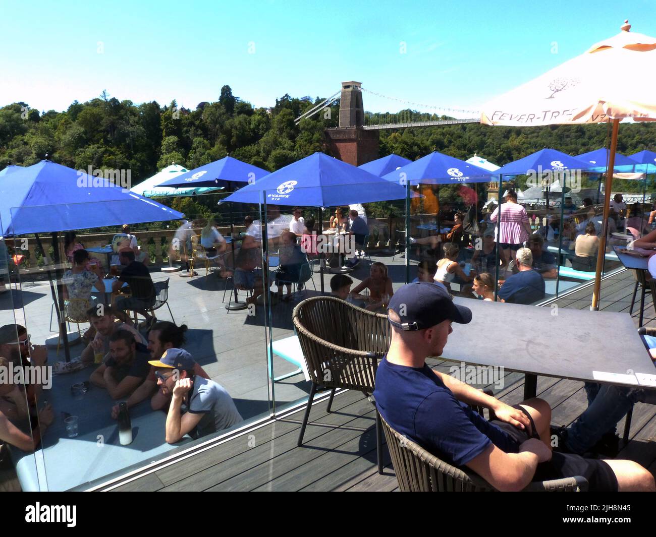 Die berühmte Clifton Suspension Bridge an einem sonnigen Sonntagnachmittag. Das ursprünglich von Isambard Kingdom Brunel entworfene und 1835 eröffnete Hotel erstreckt sich über die Avon-Schlucht über dem Fluss Avon in Clifton, Bristol. Es ist die bekannteste Struktur von Bristol und ist 365 Tage im Jahr geöffnet, mit einer Maut von £1,00, die mit einem Fahrzeug zu überqueren ist. Die Terrassenlage des Avon Gorge Hotels zieht einen konstanten Zustrom von Besuchern an, die den Blick auf dieses historische denkmalgeschützte Gebäude aus dem Jahr 1 genießen, während sie Erfrischungen unter schattigen Tischbrolles von diesem beliebten Aussichtspunkt genießen. Stockfoto