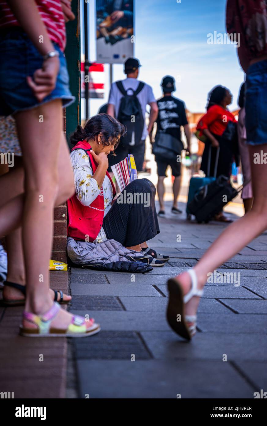 Grantham, Lincolnshire, Großbritannien – Eine junge asiatische Frau saß auf dem Straßenweg und verkaufte Kopien von The Big Issue, während die Leute an ihr vorbeigingen und sie ignorierten Stockfoto