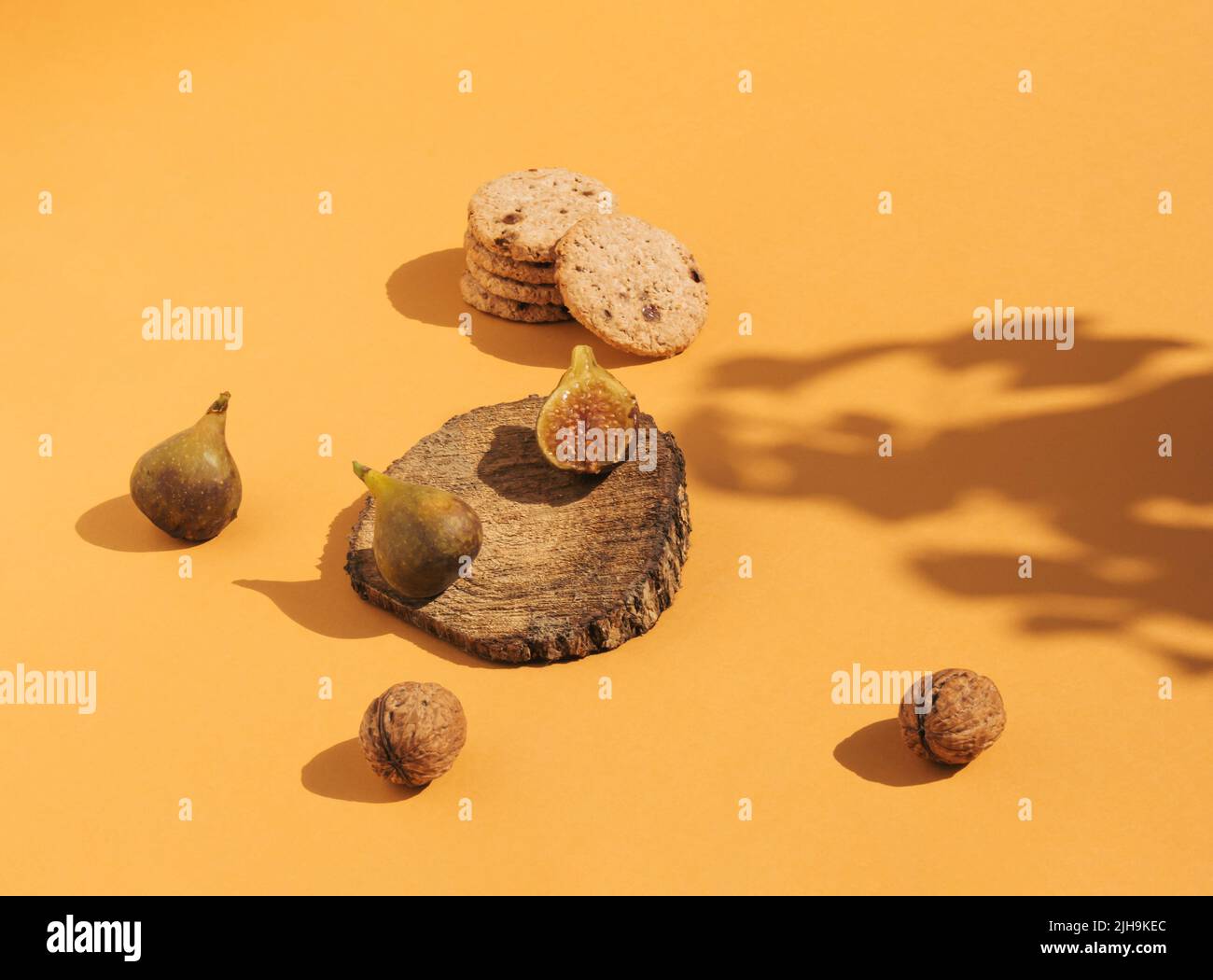 Komposition im Vintage-Stil aus Feigen auf Holzpodium, Keksen und Nüssen auf orangefarbenem Hintergrund. Retro-Food-Konzept. Stockfoto
