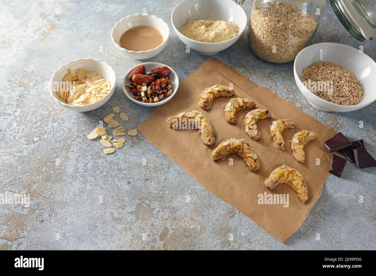 Backen gesunder Kekse aus Mandel, Haferflocken und Datteln mit dunkler Schokolade, Zutaten auf rustikalem grauen Hintergrund, Kopierraum, ausgewählter Fokus, nar Stockfoto