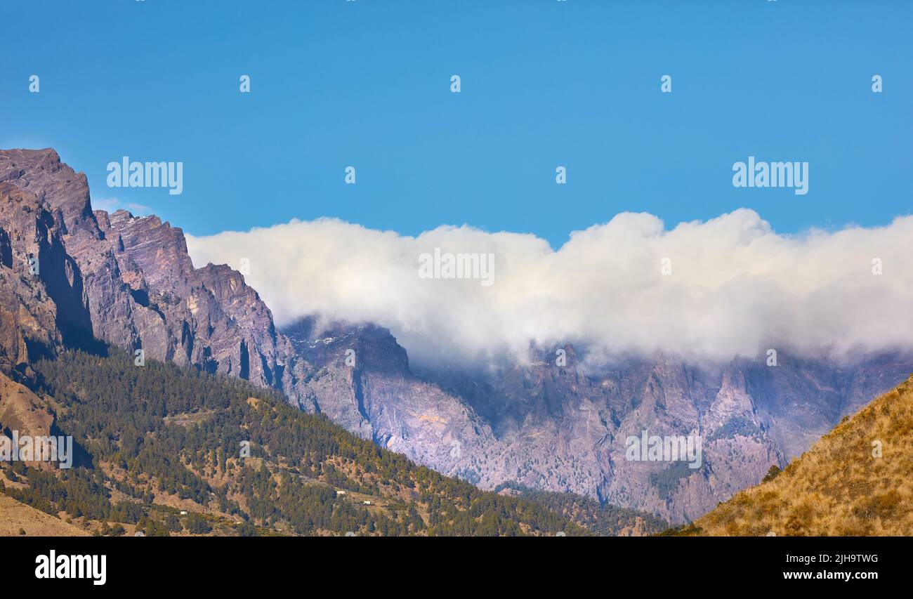 Schöne Landschaft einer Bergspitze bedeckt mit Wolken mit klarem blauen Himmel kopieren Raum oben und Hügel unten. Ein friedlicher und landschaftlich schöner Panoramablick auf Stockfoto
