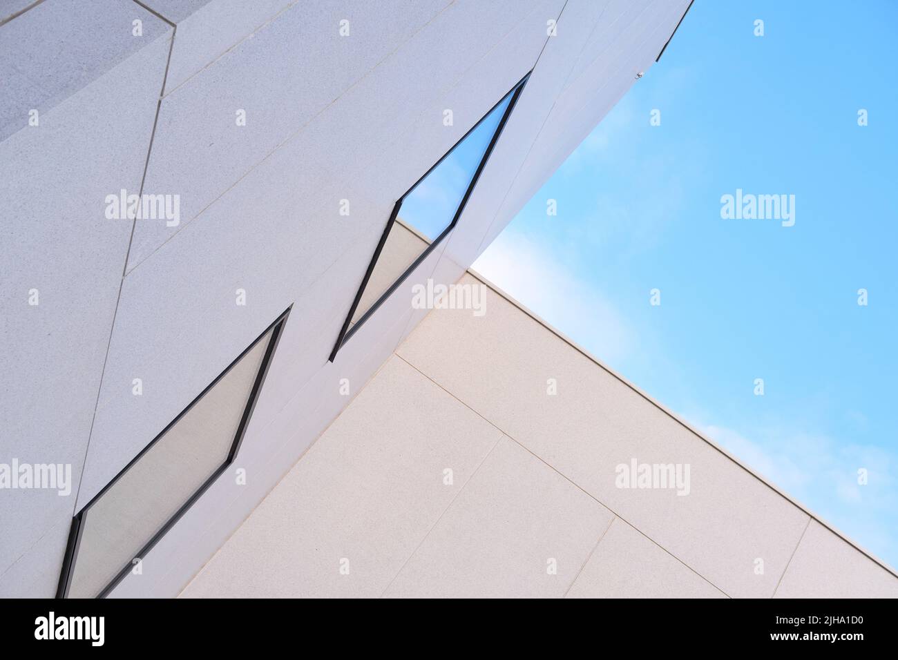 Abgewinkelte Sicht auf das Äußere eines hohen Gebäudes an einem sonnigen Tag. Konzept eines modernen weißen Gehäuses mit reflektierenden Fenstern vor einem blauen Himmel. Abstrakter Hintergrund Stockfoto