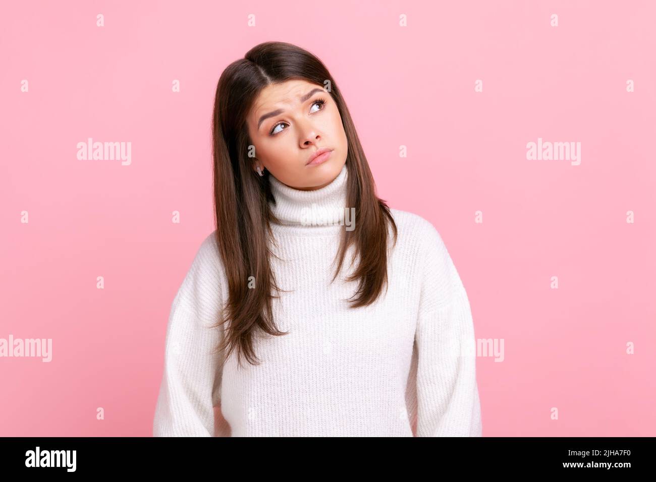 Verwirrt puzzles Frau nachdenklich weg mit nachdenklichen Ausdruck, Entscheidungen treffen, lösen Dilemma, tragen weißen lässigen Stil Pullover. Innenaufnahme des Studios isoliert auf rosa Hintergrund. Stockfoto