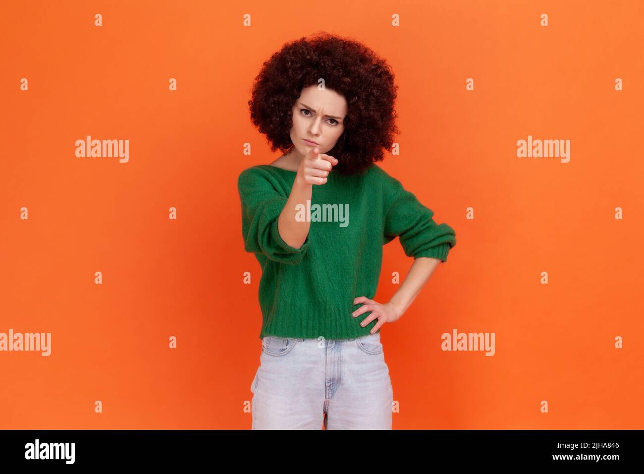 Porträt einer strengen Frau mit Afro-Frisur, die mit dem Zeigefinger auf die Kamera zeigt und einen ernsten ermahnenden Gesichtsausdruck hat. Innenaufnahme des Studios isoliert auf orangefarbenem Hintergrund. Stockfoto