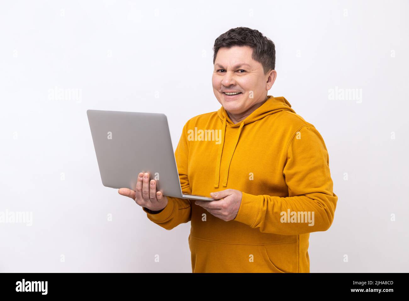 Porträt eines Mannes, der am Laptop E-Mails tippt oder im sozialen Netzwerk chattet, mit fröhlichem Gesichtsausdruck auf die Kamera blickt und einen Hoodie im urbanen Stil trägt. Innenaufnahme des Studios isoliert auf weißem Hintergrund. Stockfoto