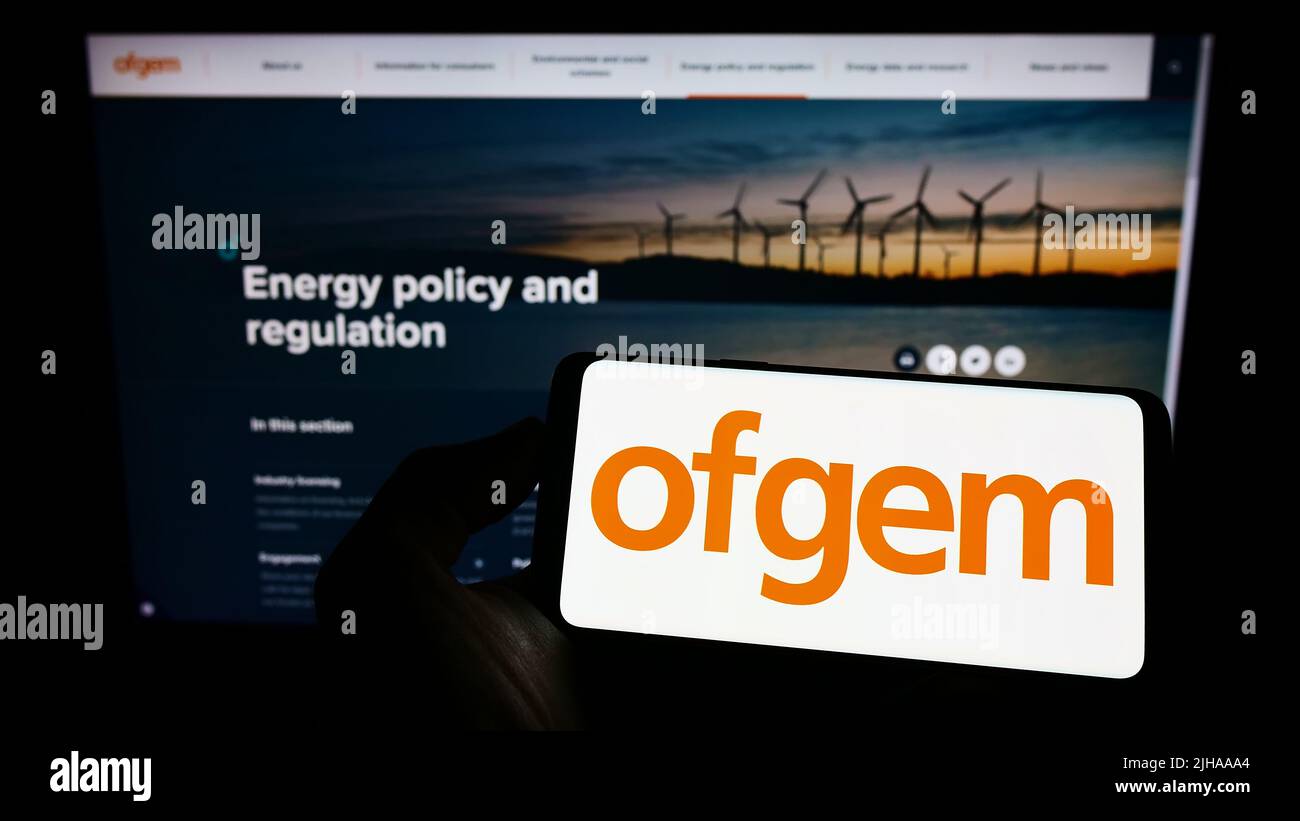 Person, die ein Mobiltelefon mit dem Logo des Amtes für Gas- und Elektrizitätsmärkte (Ofgem) auf dem Bildschirm vor der Webseite hält. Konzentrieren Sie sich auf die Telefonanzeige. Stockfoto