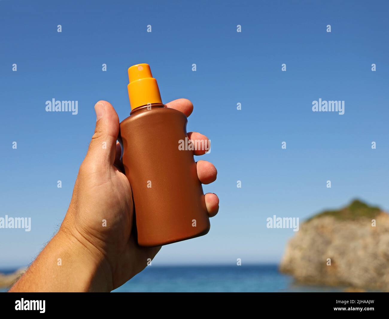 Männliche Hand hält eine Sprühflasche mit Sonnenschutzcreme am Meer, wichtiger Sonnenschutz im Urlaub Stockfoto
