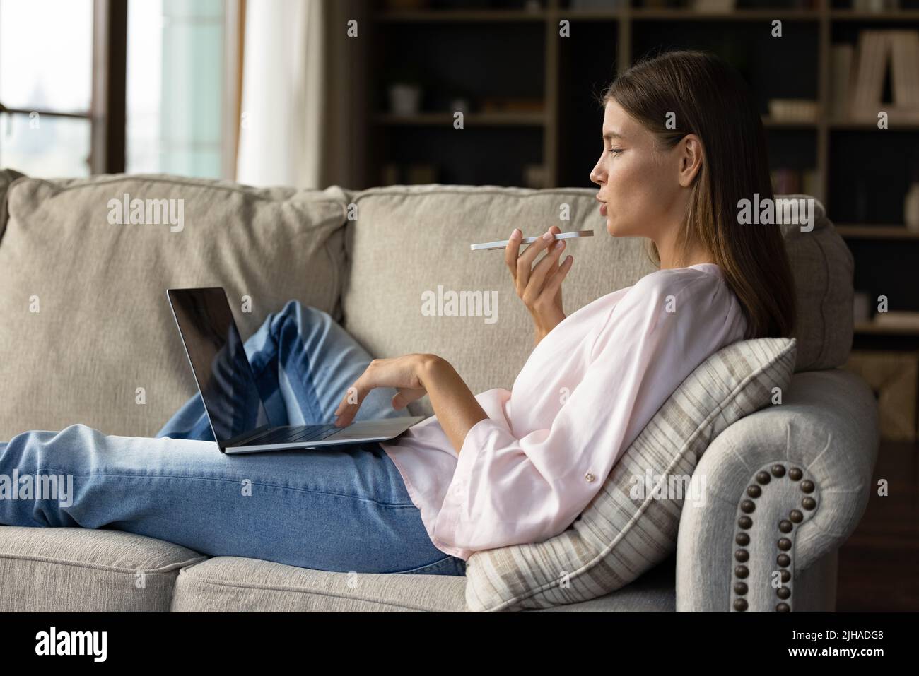 Frau führt Telefongespräche über Freisprecheinrichtung und mit einem Laptop in der Halle Stockfoto