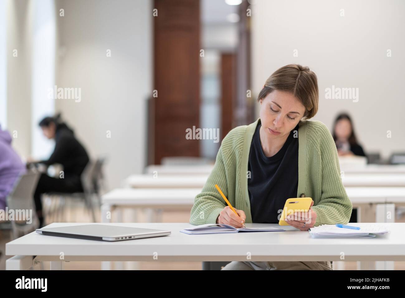 Konzentrierte reife Studentin, die Smartphone für die Prüfungsvorbereitung verwendet und den zweiten Abschluss macht Stockfoto