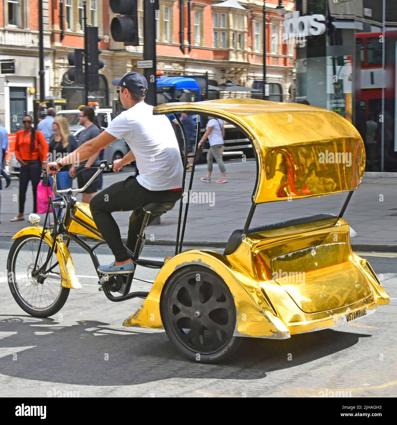 Leeres, goldfarbenes Rikscha-Dreirad und Fahrer, der Kunden sucht, die entlang des Londoner West End, der Oxford Street, dem Einkaufs- und Touristenviertel, England, fahren Stockfoto