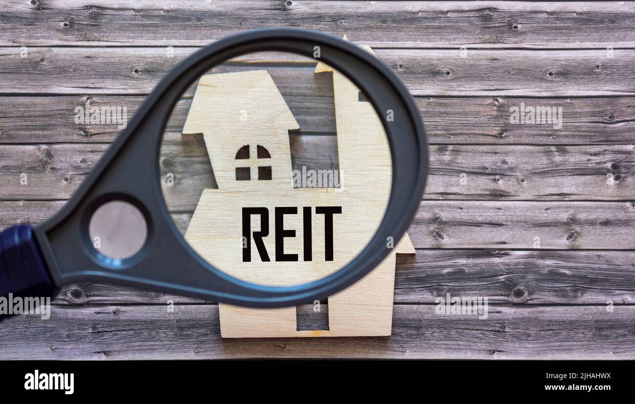 Real Estate Investment Trust REIT-Konzept, Text durch eine Lupe auf ein Hausmodell Stockfoto